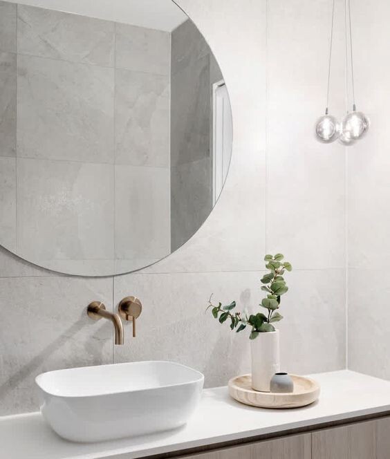 Round mirror above washbasin area, white basin, brass fittings, plant on wooden surface