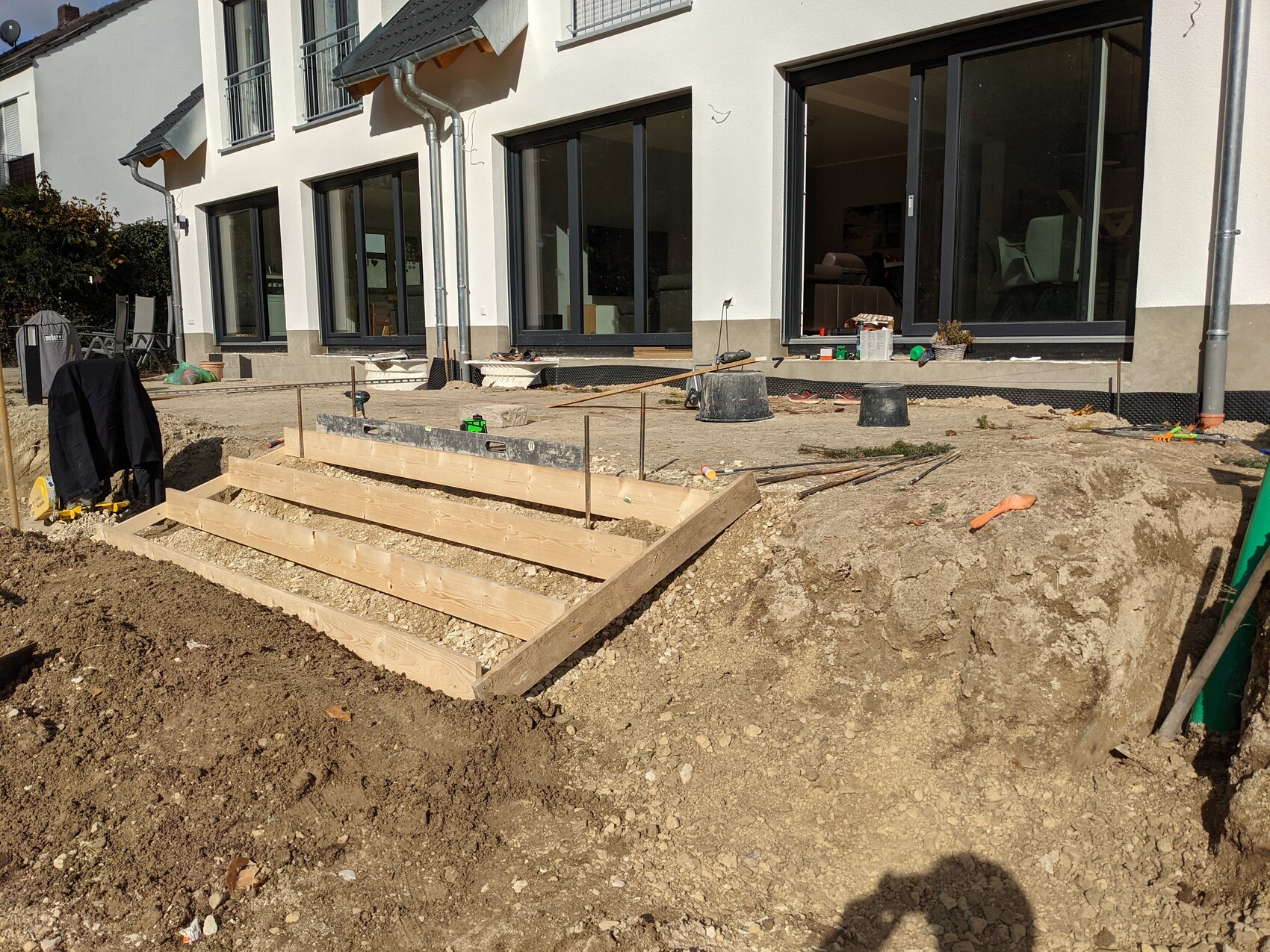 Baustelle vor Wohnhaus: Holzstufenbau, Erdreich, Werkzeuge, Eimer und Bretter liegen bereit.
