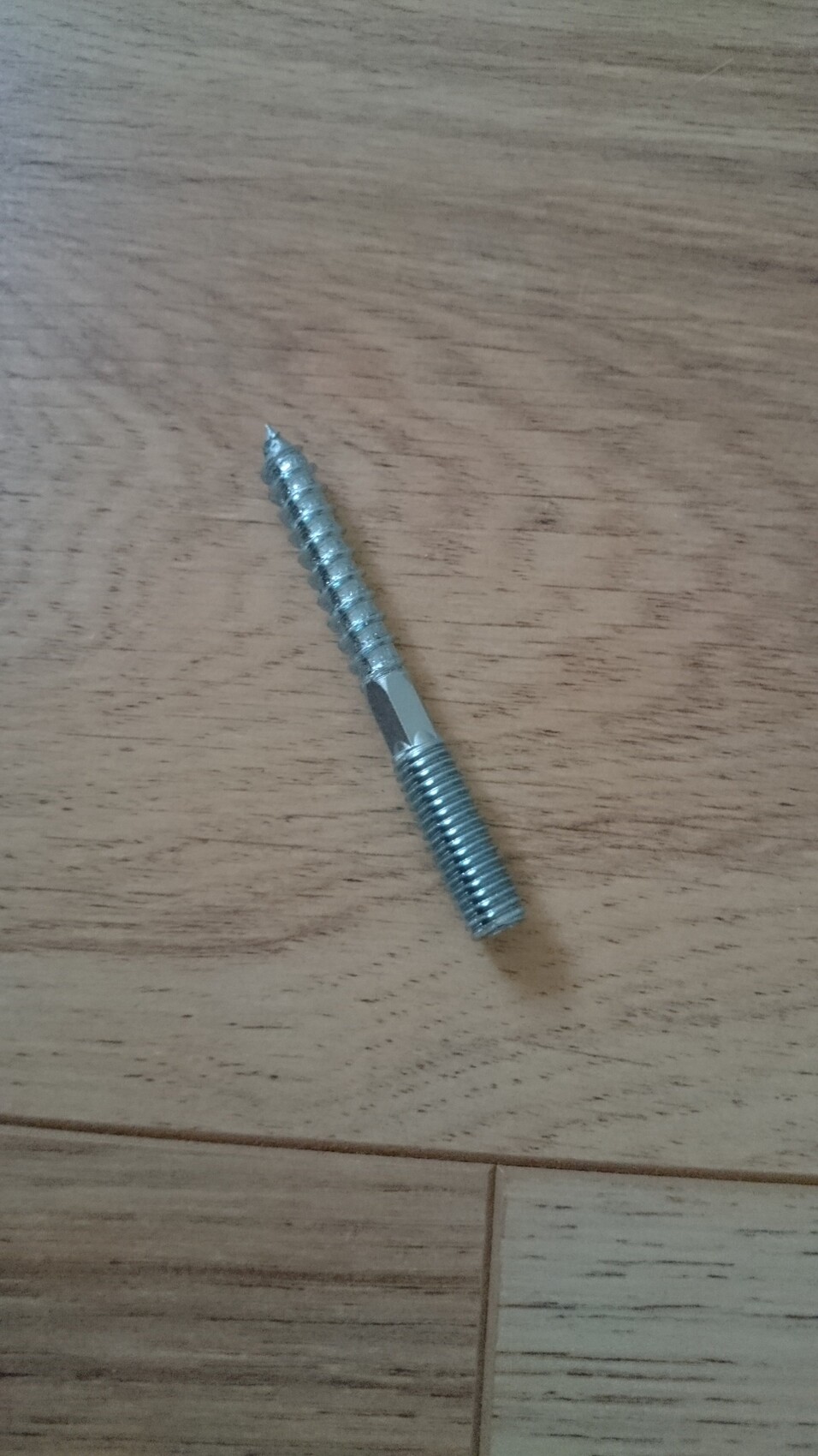 Eine silberne Metall-Schraube liegt auf einem Holzboden