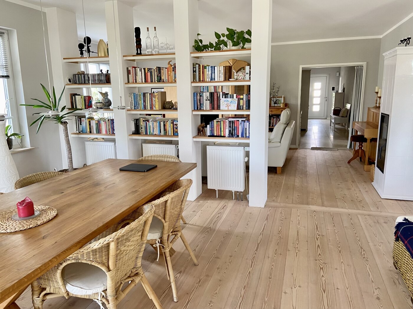 Heller Essbereich mit Holztisch, Korbsesseln und Bücherregalen, Blick ins Wohnzimmer.