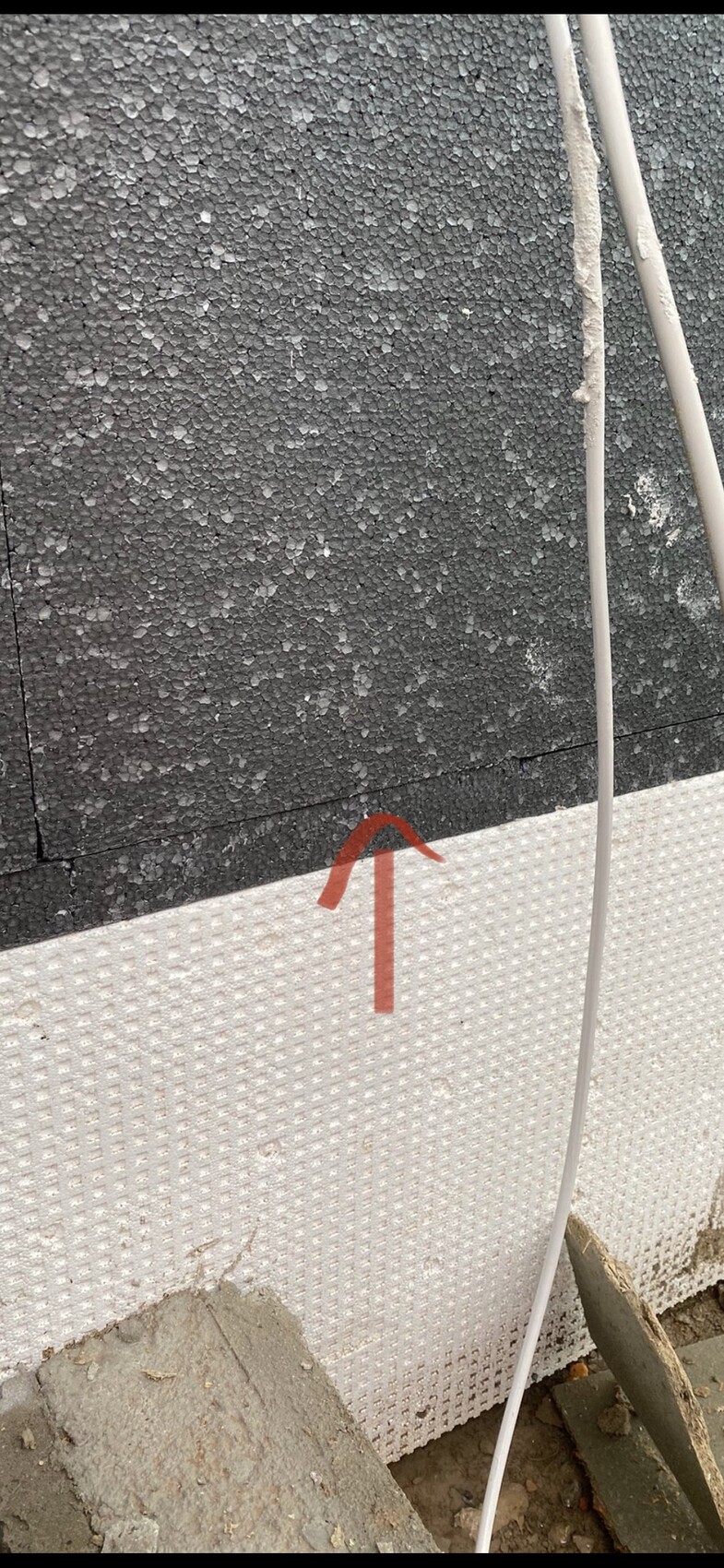 Exterior wall with black, rough insulation surface; white insulation boards at the bottom; red arrow marking a joint.