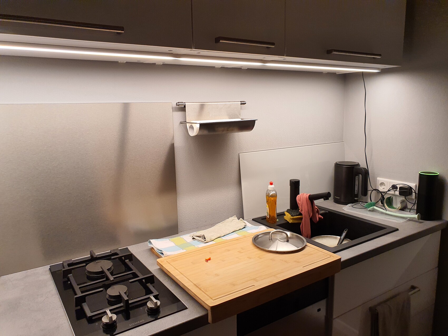 Kitchen with gas stove on the left, sink on the right, cutting board, dish soap, and kettle.