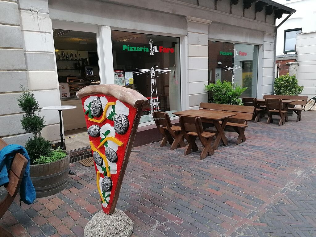 Outdoor area of a pizzeria: wooden tables, benches, large pizza decoration in front of the entrance.