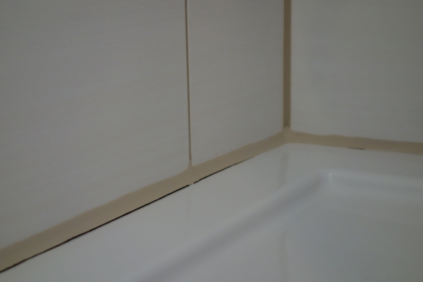 Close-up of a bathroom wall tile corner above the white bathtub; beige grout with gap.