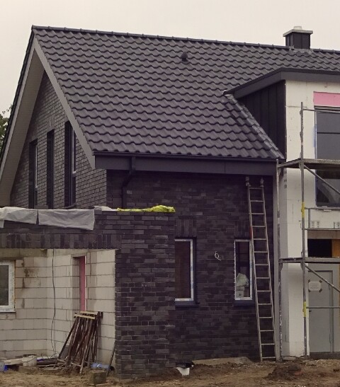 Two-story house under construction with dark brick facade, scaffolding, and ladder.