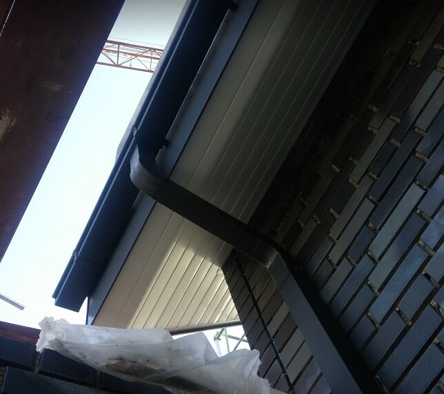 Exterior view of a construction site with gray gutter on dark brick wall