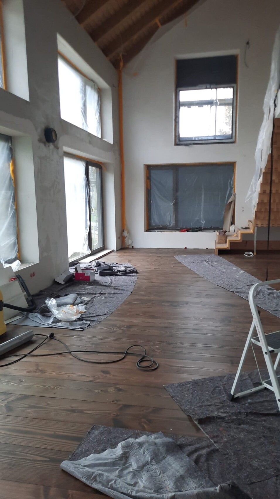 Bright open shell room with wooden floor, large windows, protective tarps, and tools.