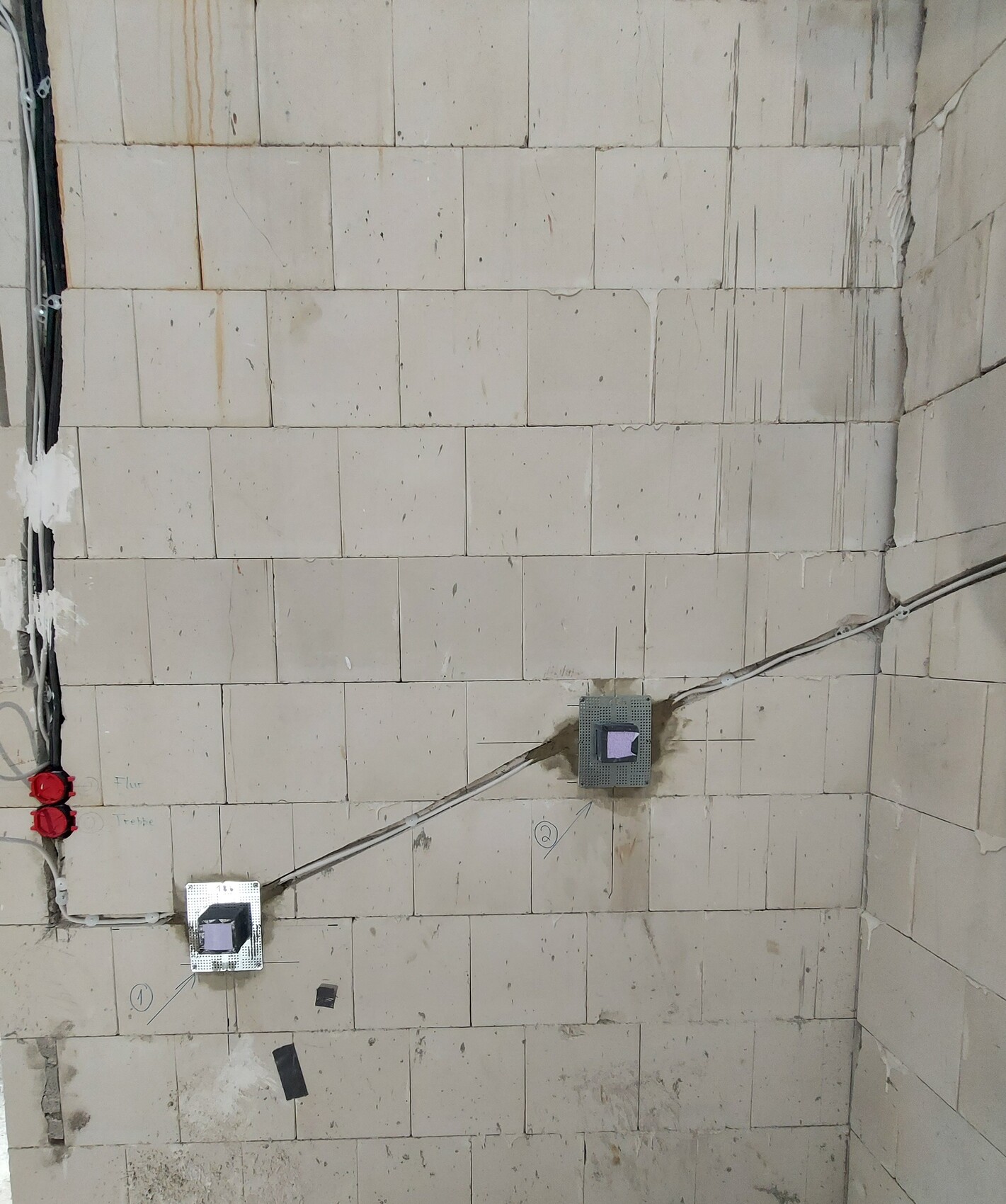 White tiled wall with two square boxes and diagonally running cables