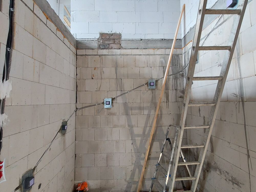 Construction site: tiled walls, visible cables, outlet boxes, and a ladder leaning against the wall.