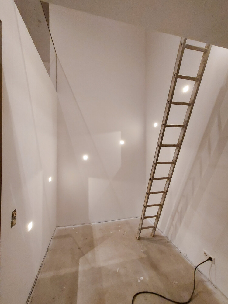 Unfinished construction space: light walls, ladder leaning against the wall, cables on the floor.
