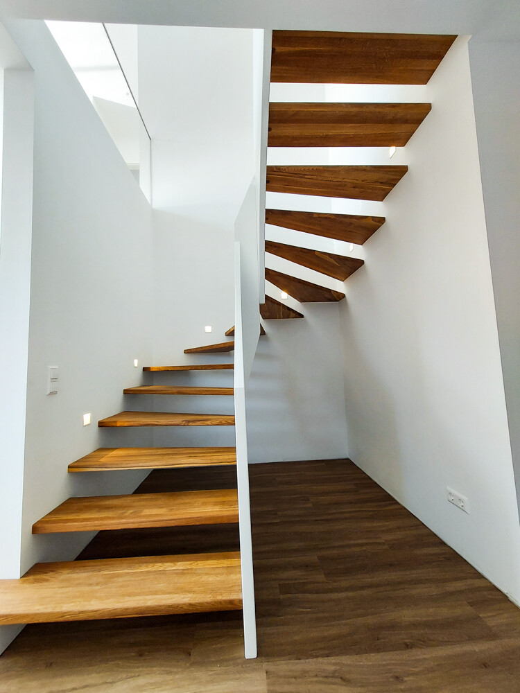 Modern interior: two floating wooden staircases in front of white walls and dark wood flooring.