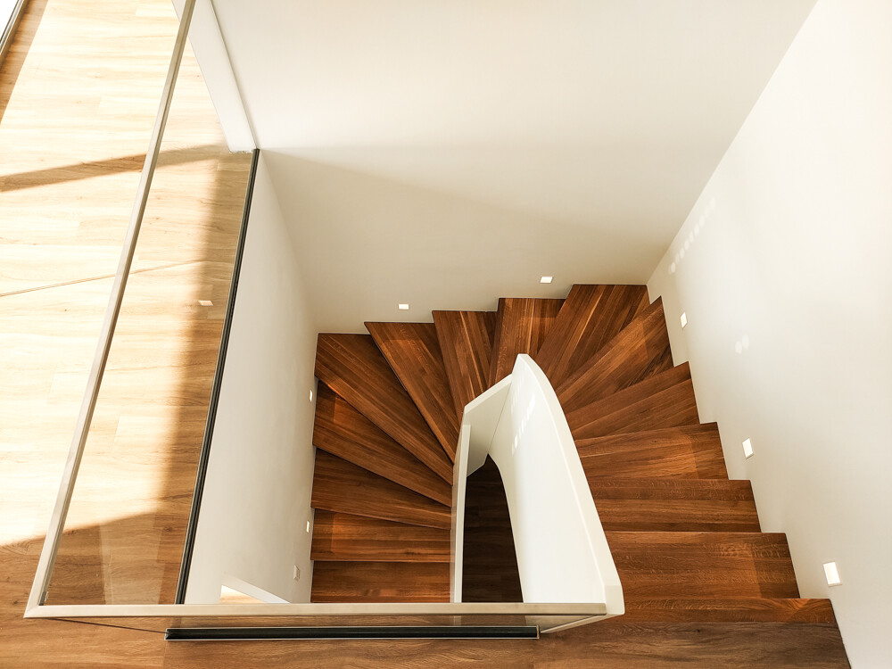 Spiral wooden staircase with white railing, top view in a bright modern interior.