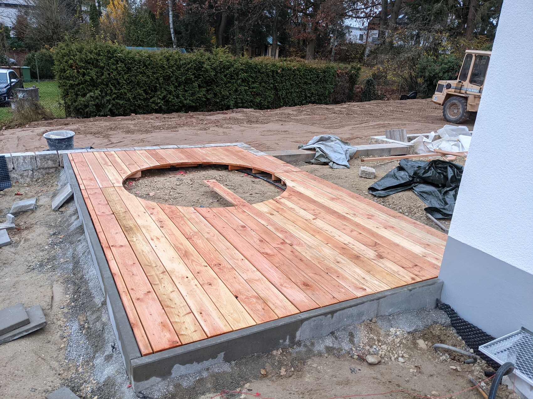 Wooden deck with circular opening in the garden, excavator in the background.