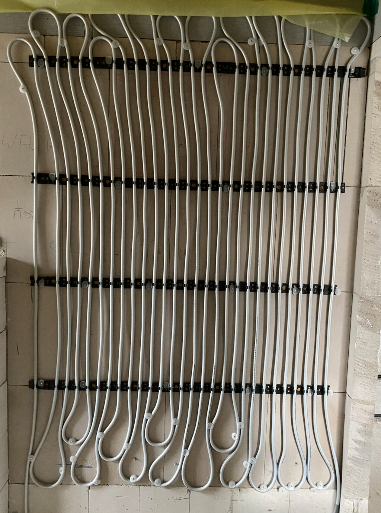 Many white heating cables mounted on a wall, ready for underfloor heating.