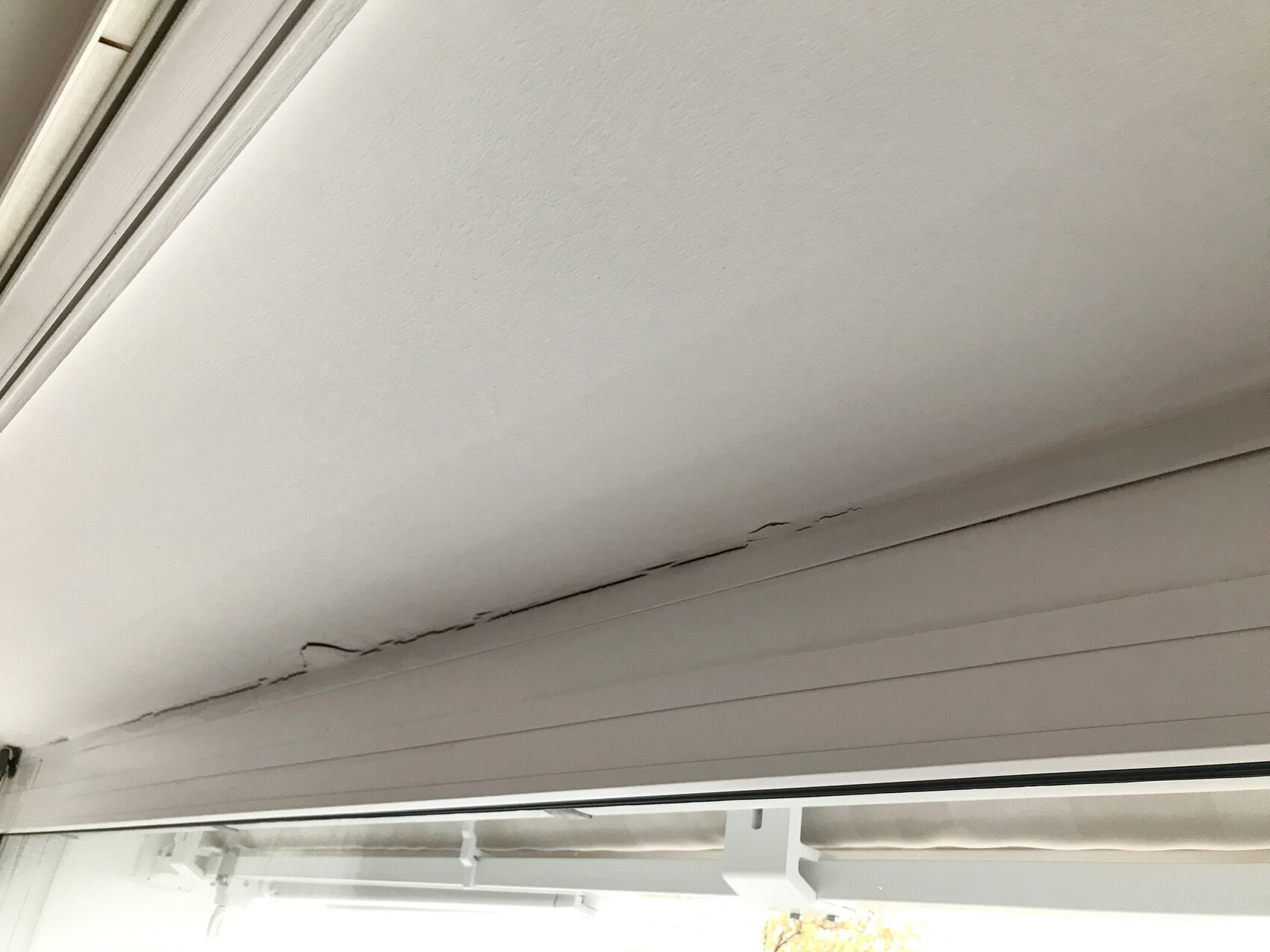 Crack in the ceiling area above the window frame inside a room.