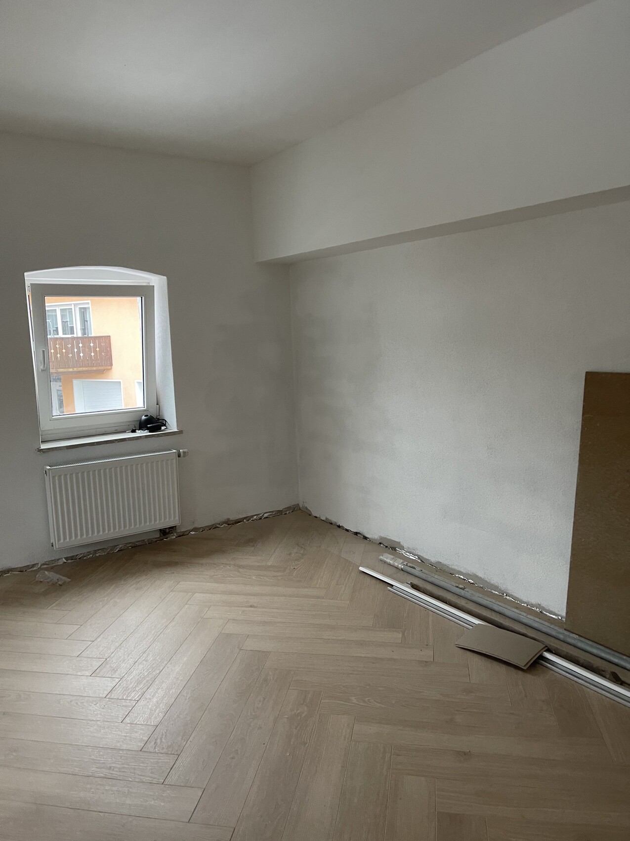 Empty room under renovation with window, radiator, and construction materials on the floor.