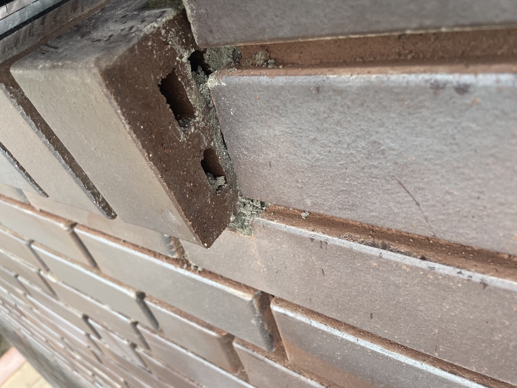 Close-up of a damaged brick in a brown wall with a hole and dust.