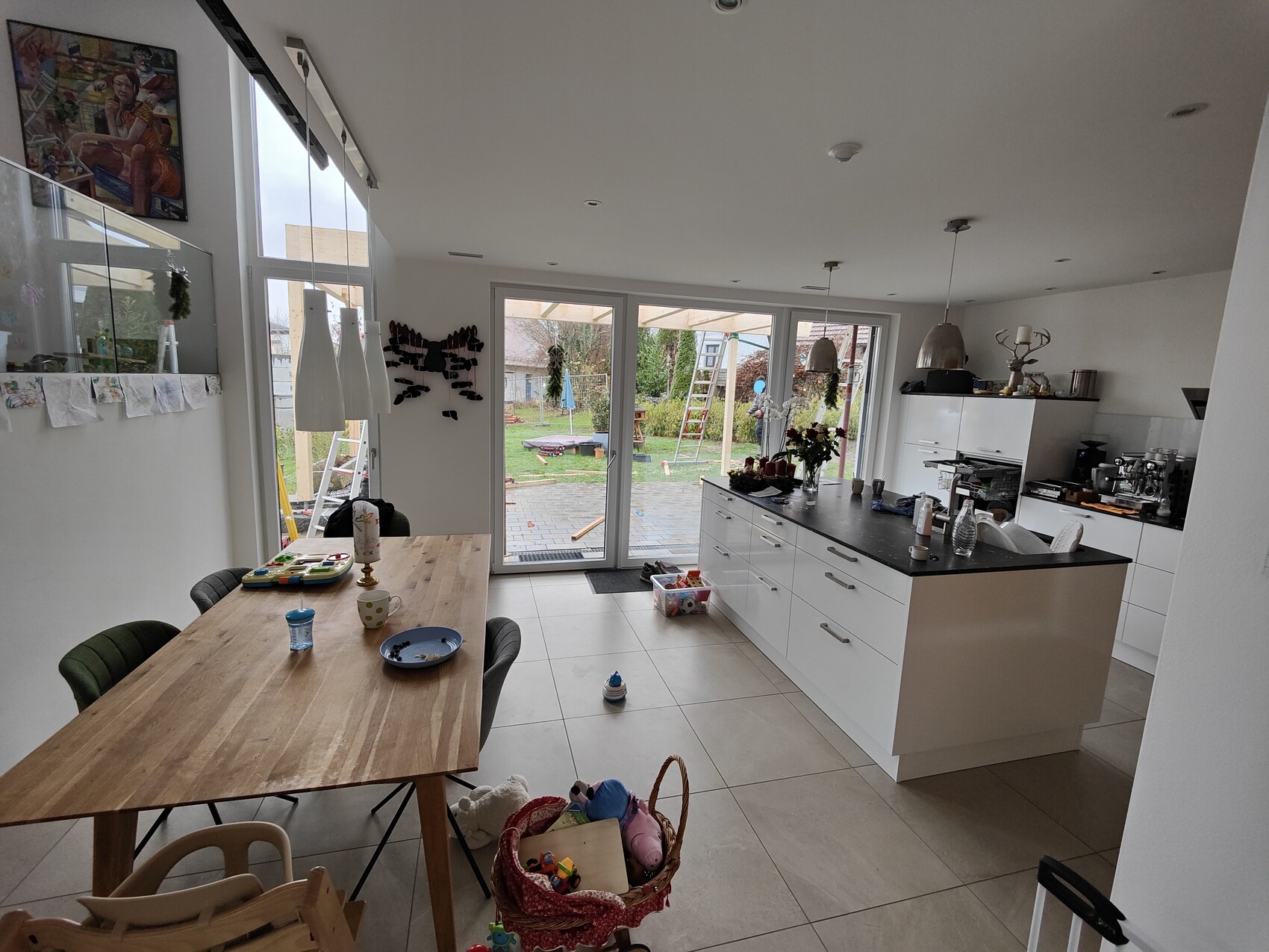 Modern kitchen with island, dining table, toy basket; view of garden through glass front.