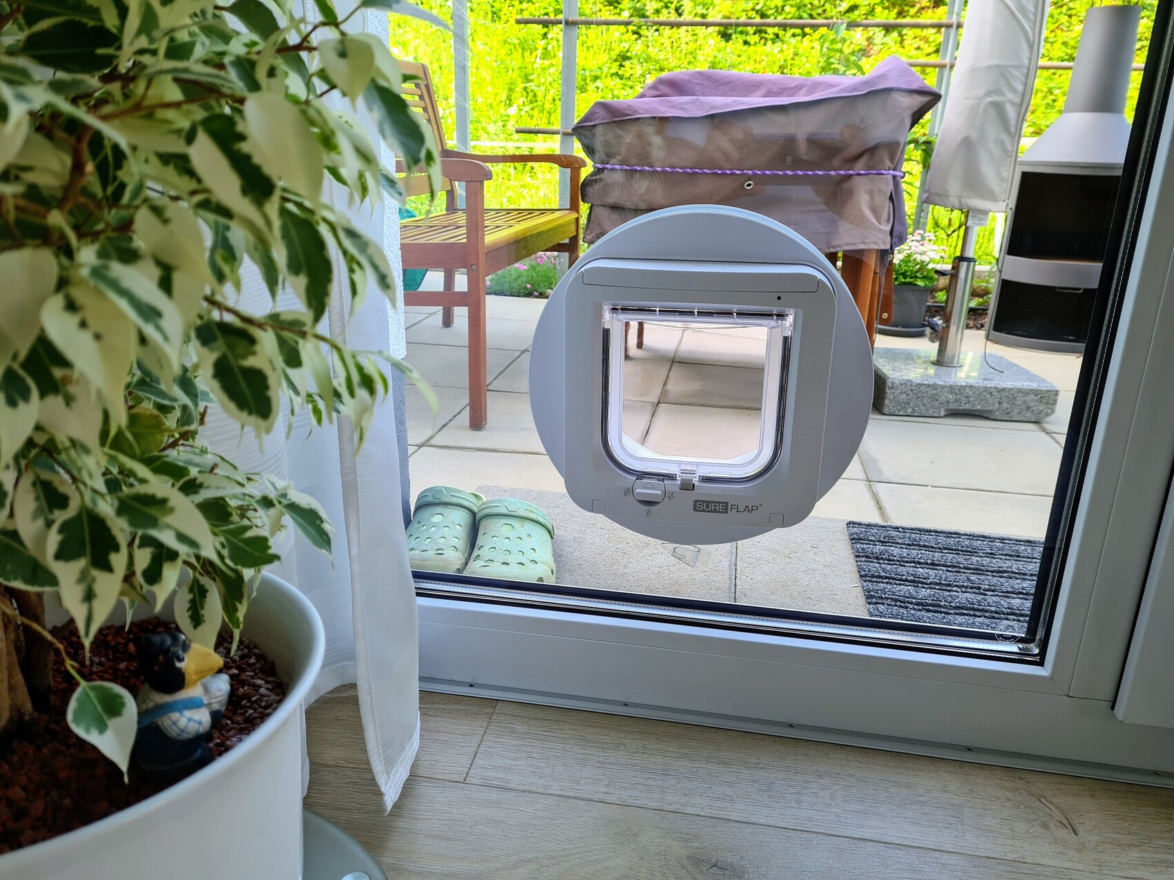 Round pet flap in glass sliding door; view towards terrace with garden furniture.