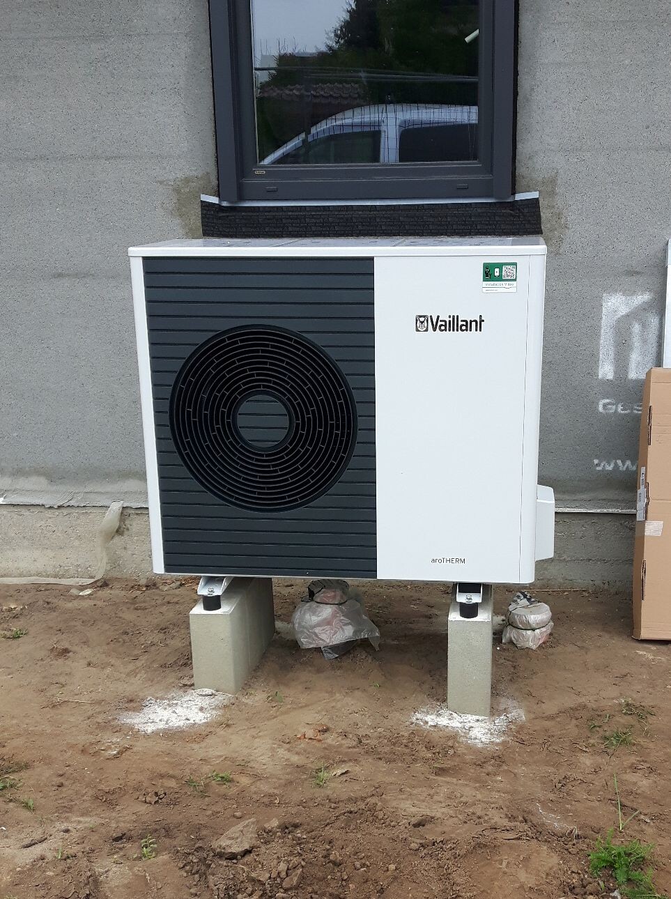 Outdoor unit of the Vaillant aroTHERM heat pump on concrete blocks in front of the house wall.