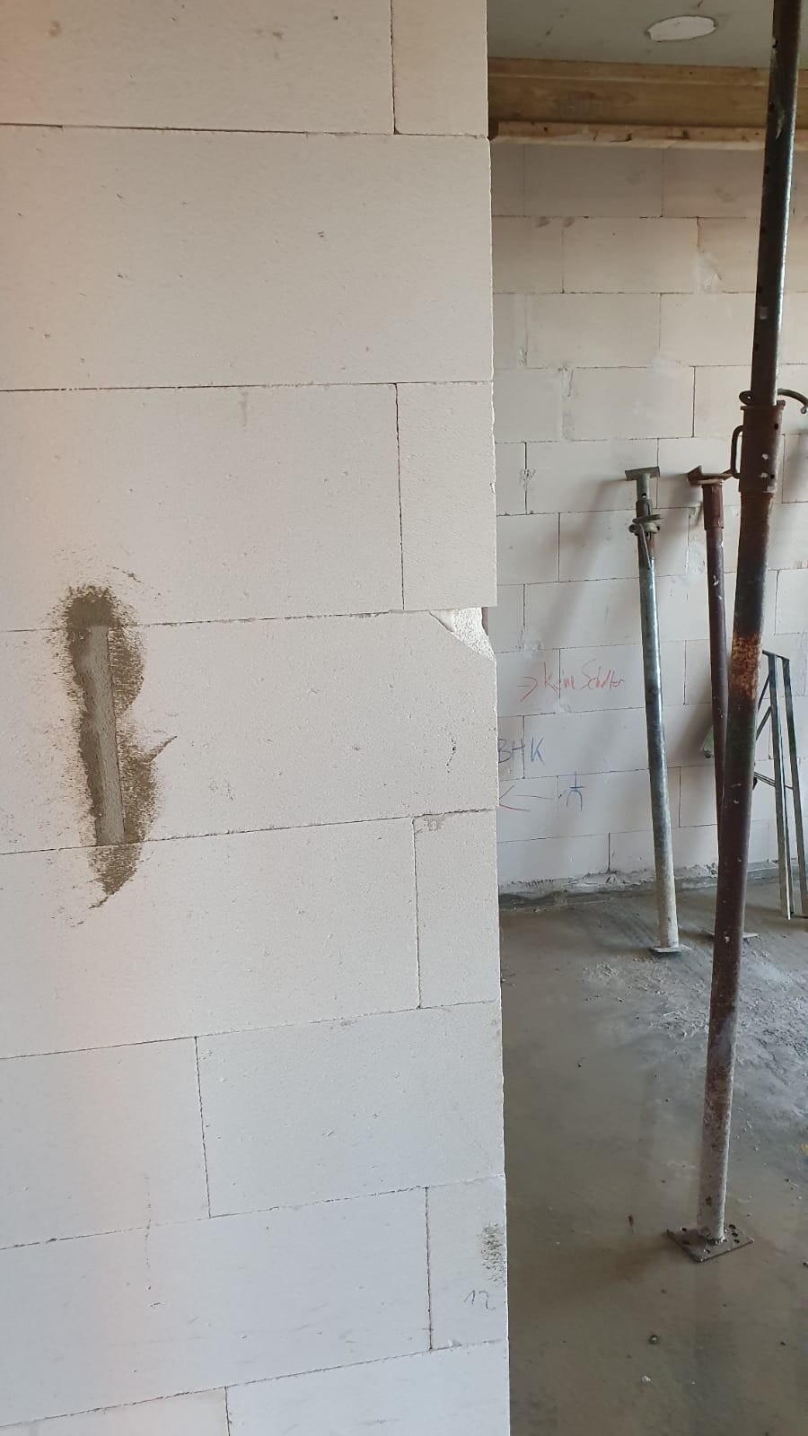 Interior of a construction site with a white block wall, rusty steel supports, and mortar traces.