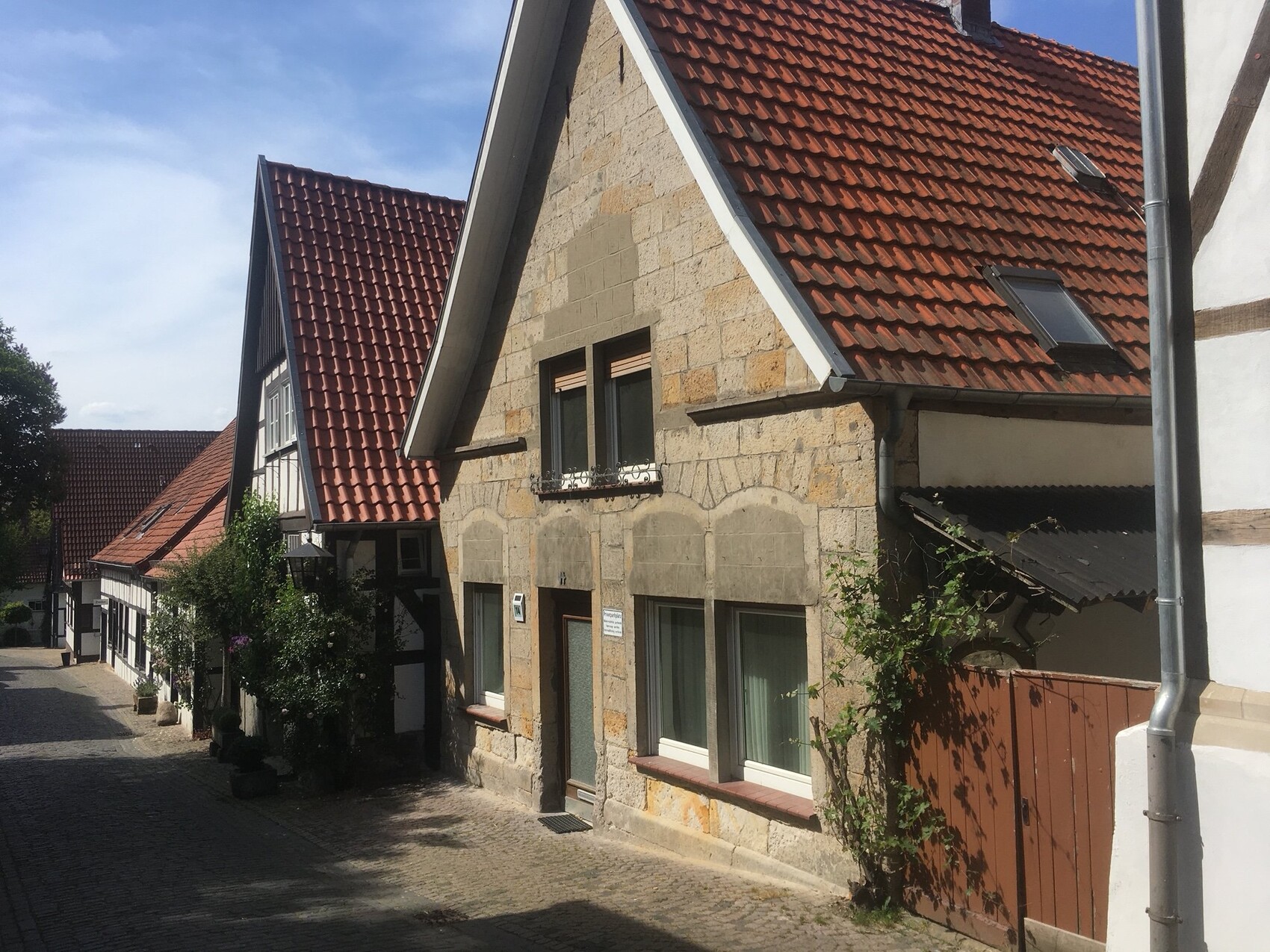 Row of historic houses with red tiled roofs, stone facades, and cobblestone pavement.
