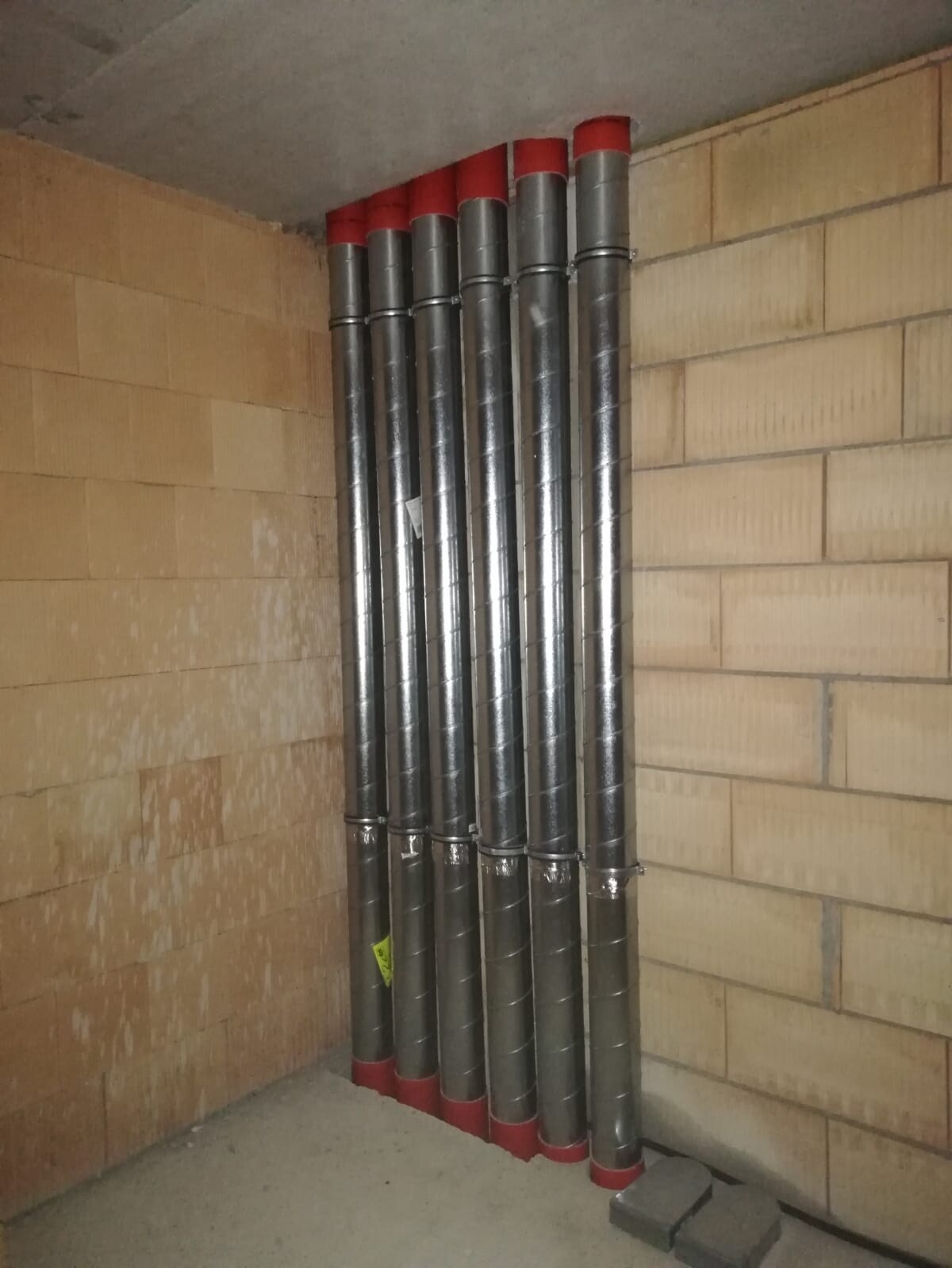 Mehrere vertikale Metallrohre mit roten Kopfkappen im Keller neben Ziegelwand
