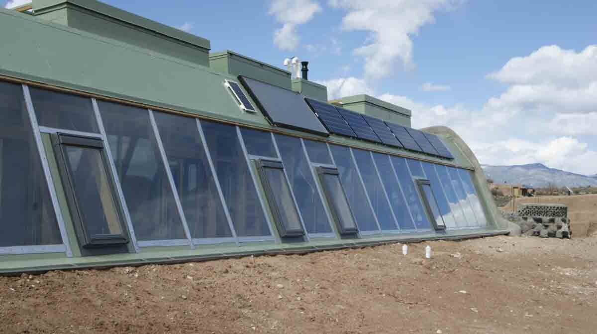 Long greenhouse with large windows and solar panels on the roof in dry landscape.
