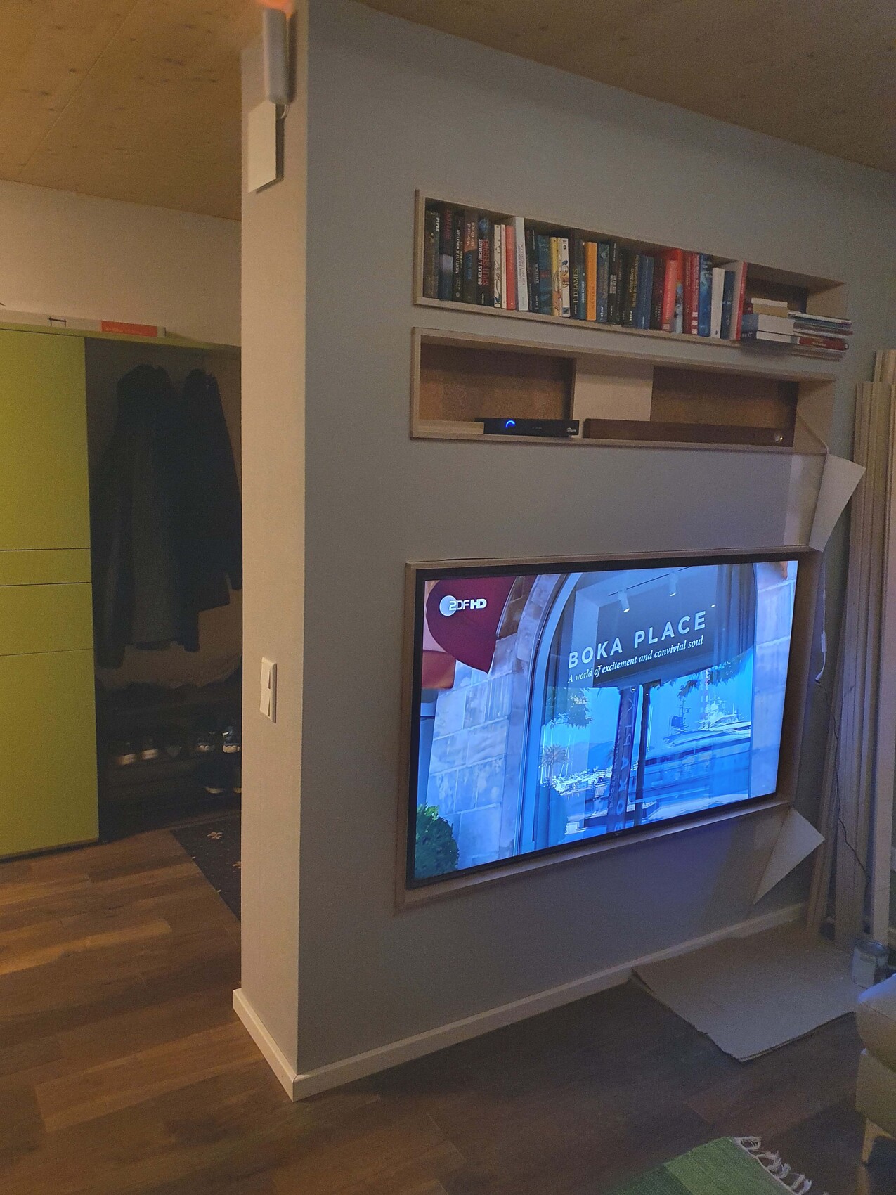 Living room: TV in wall niche, bookshelf above; wardrobe on the left with jackets.
