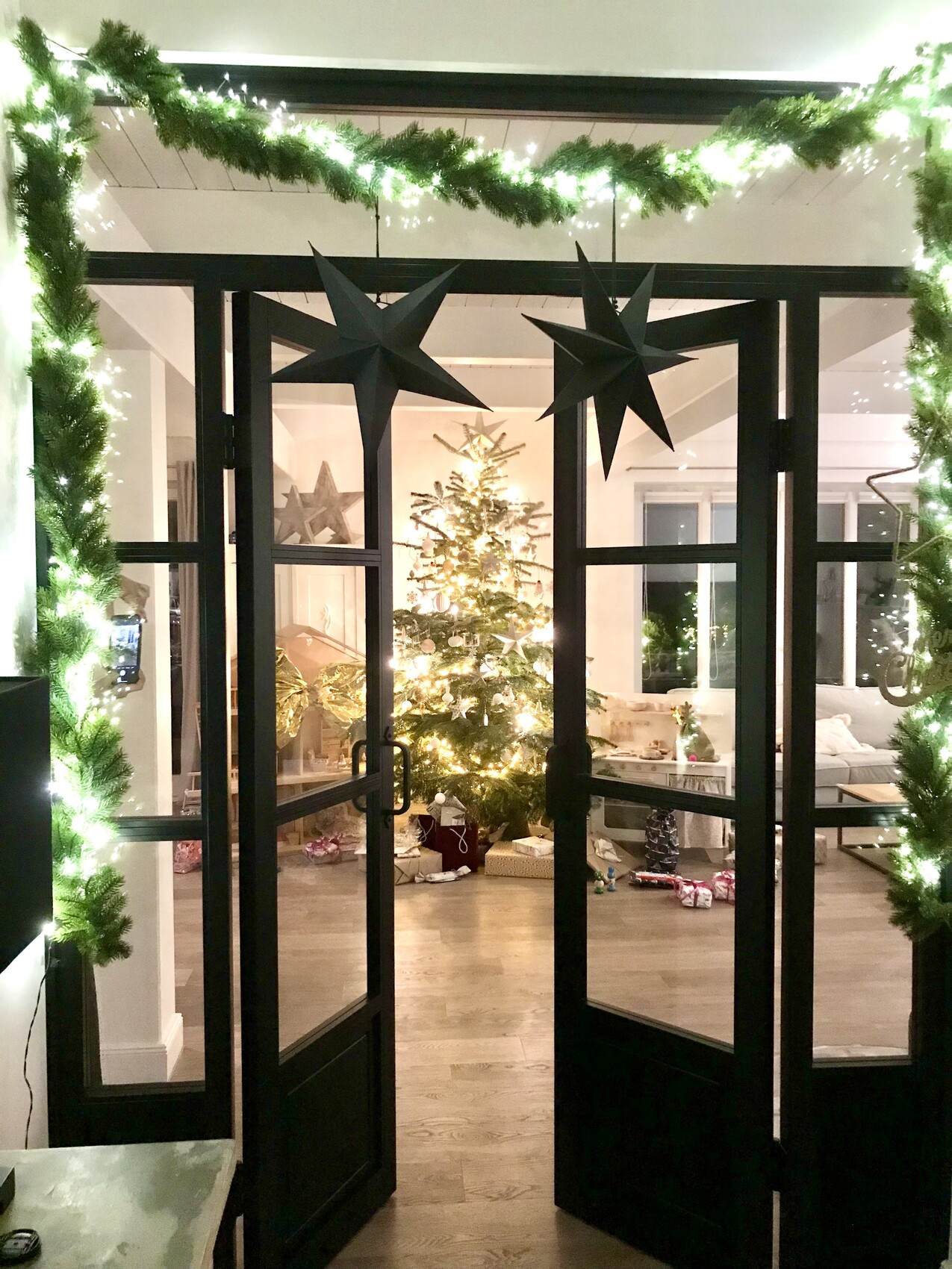 Open glass door with green string lights; interior with Christmas tree and presents.