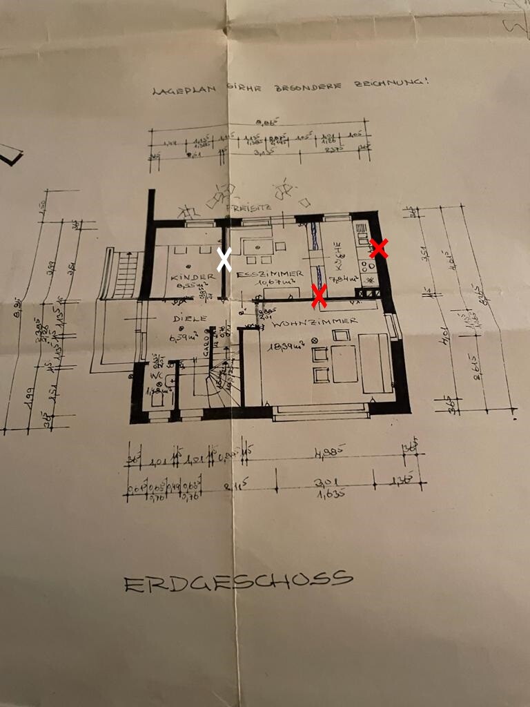 Grundriss Erdgeschoss eines Hauses mit Wohnzimmer, Küche, Kinderzimmer; zwei rote X-Markierungen.