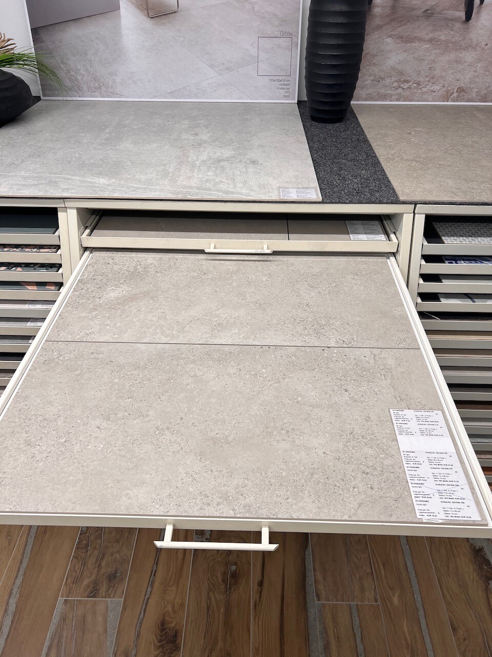 Showroom shelf with pull-out tile samples in shades of gray and wood flooring underneath