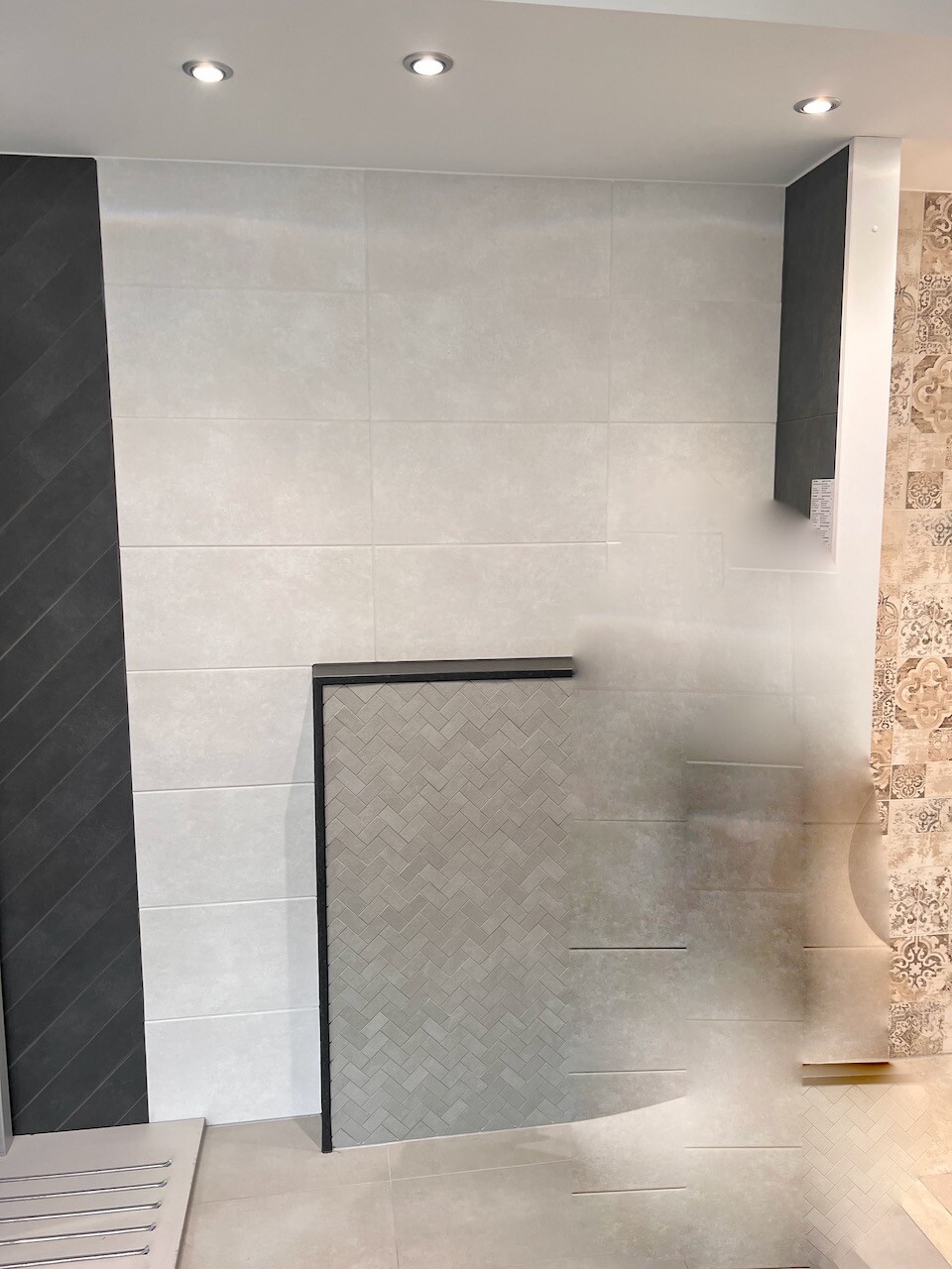 Bathroom showroom with light gray tiles, black frame, niche shower with zigzag pattern.