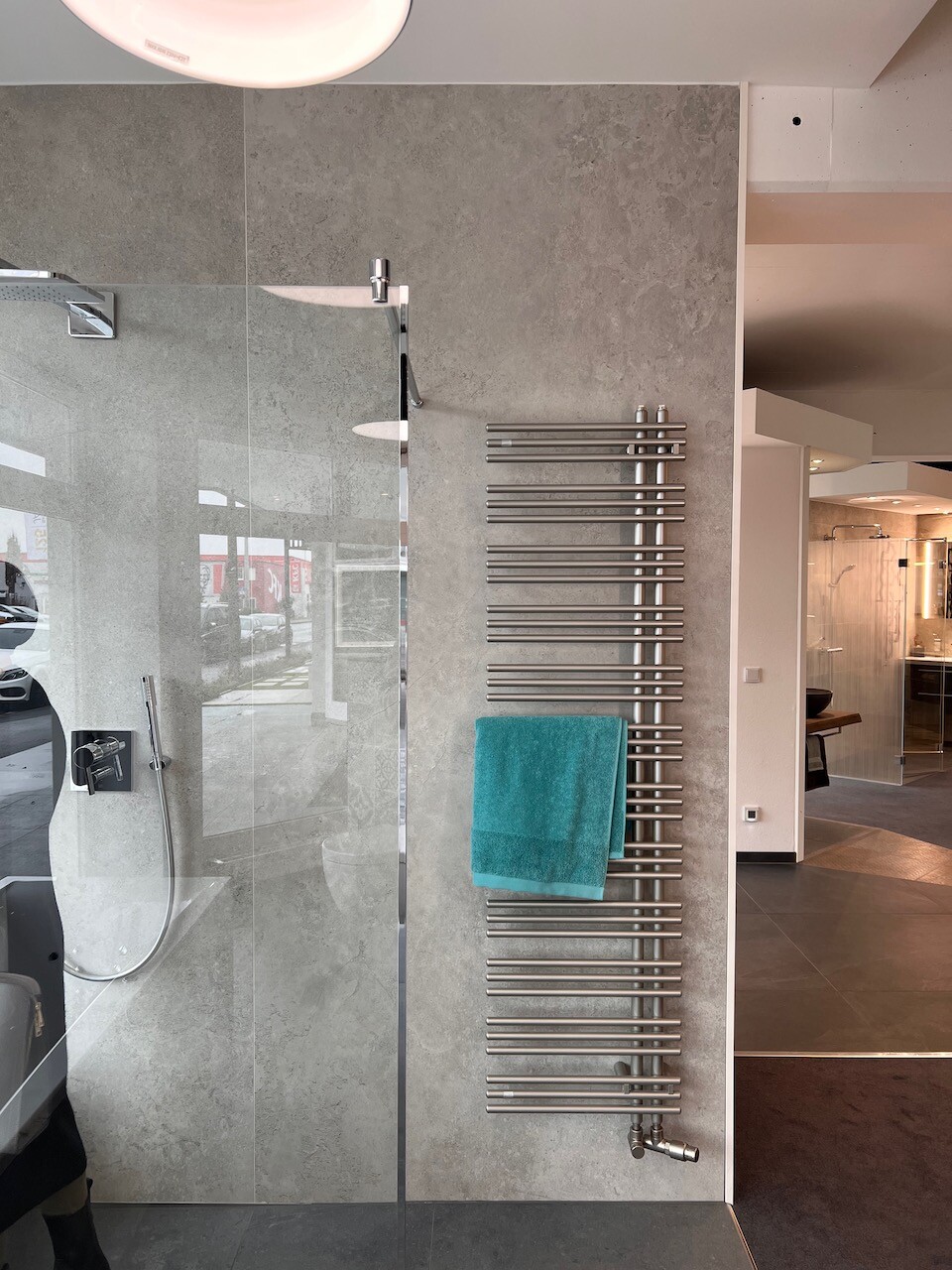 Modern shower with glass wall on the left, next to radiator with turquoise towel.