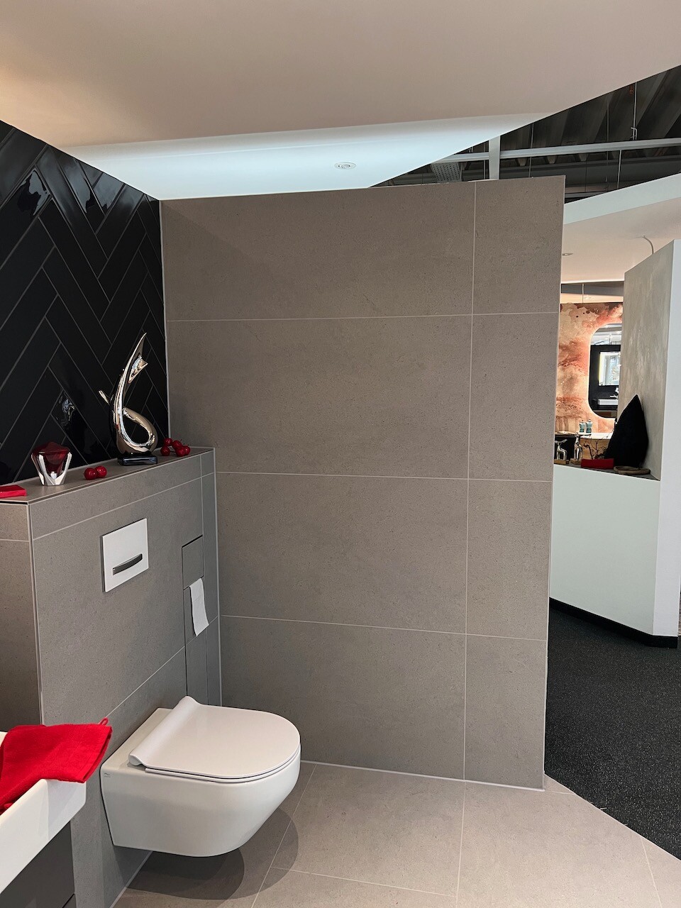 Modern bathroom with wall-hung toilet, gray tiles, and red decoration on the cistern.