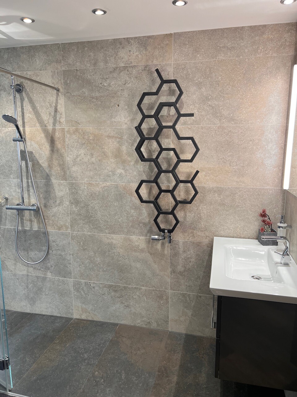 Modern bathroom with gray tiles, shower on the left, black hexagon wall decoration.