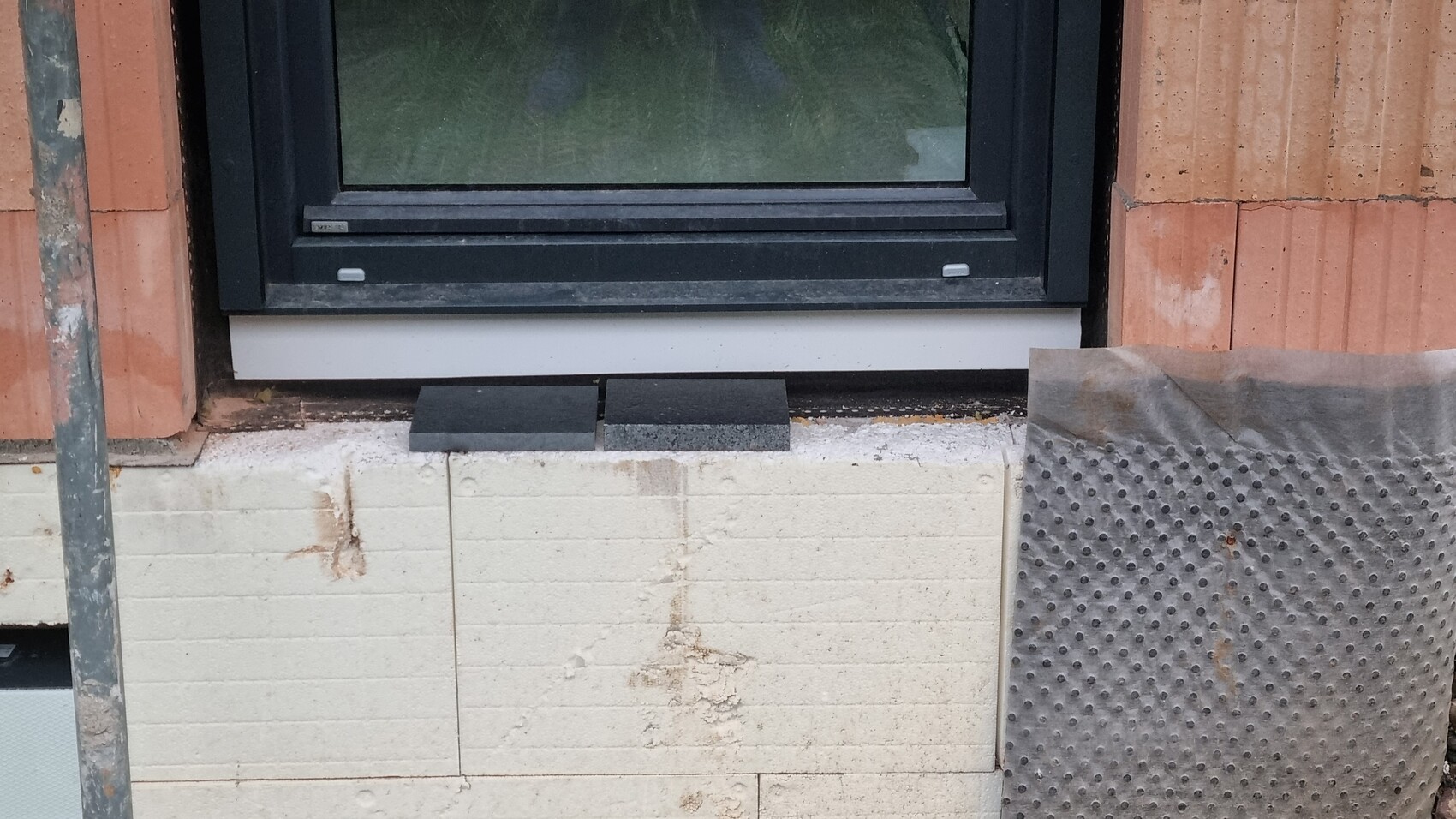Window frame in unfinished exterior wall with stone cladding and construction work
