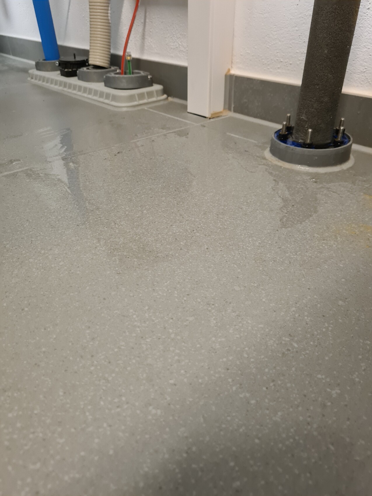 Grey speckled epoxy floor in a workshop; pipes and support posts visible.