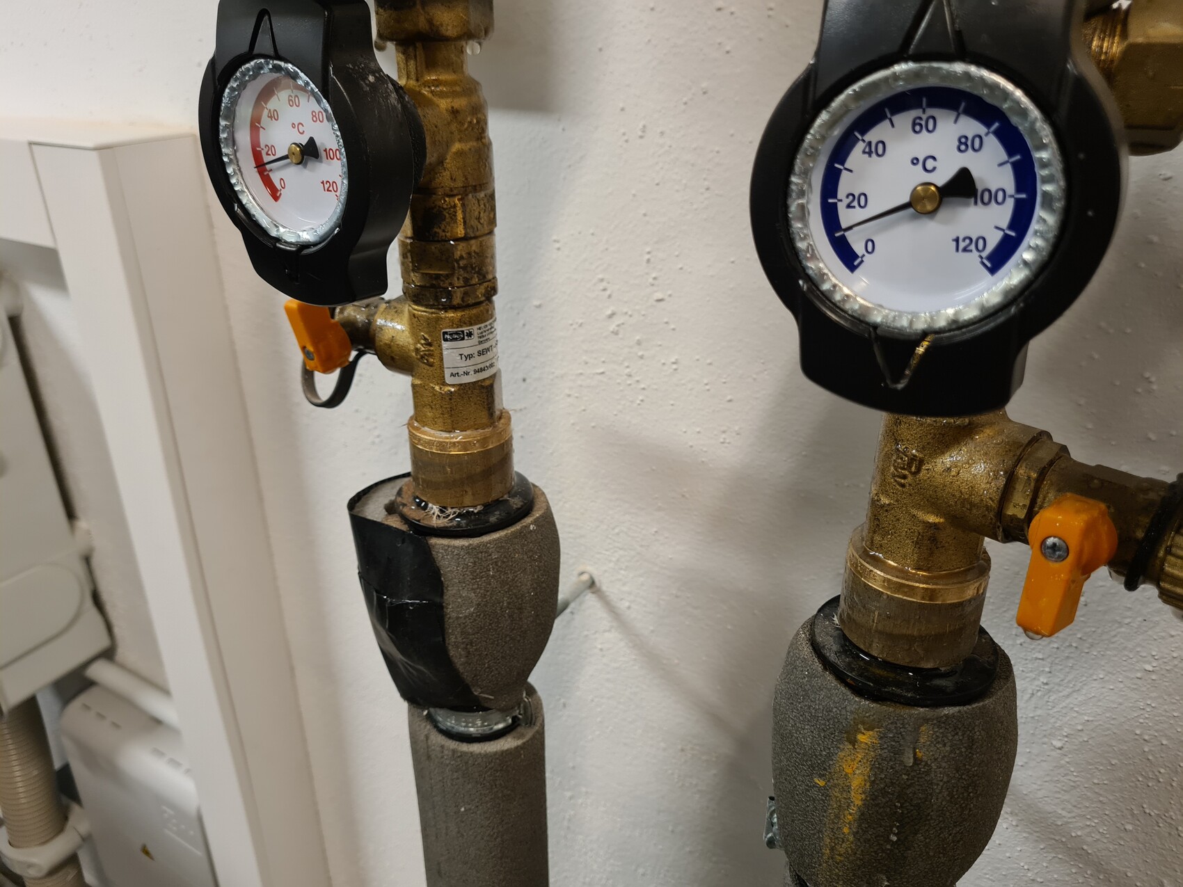 Two gauges (pressure/temperature) on heating pipes with orange shut-off valves and insulation.