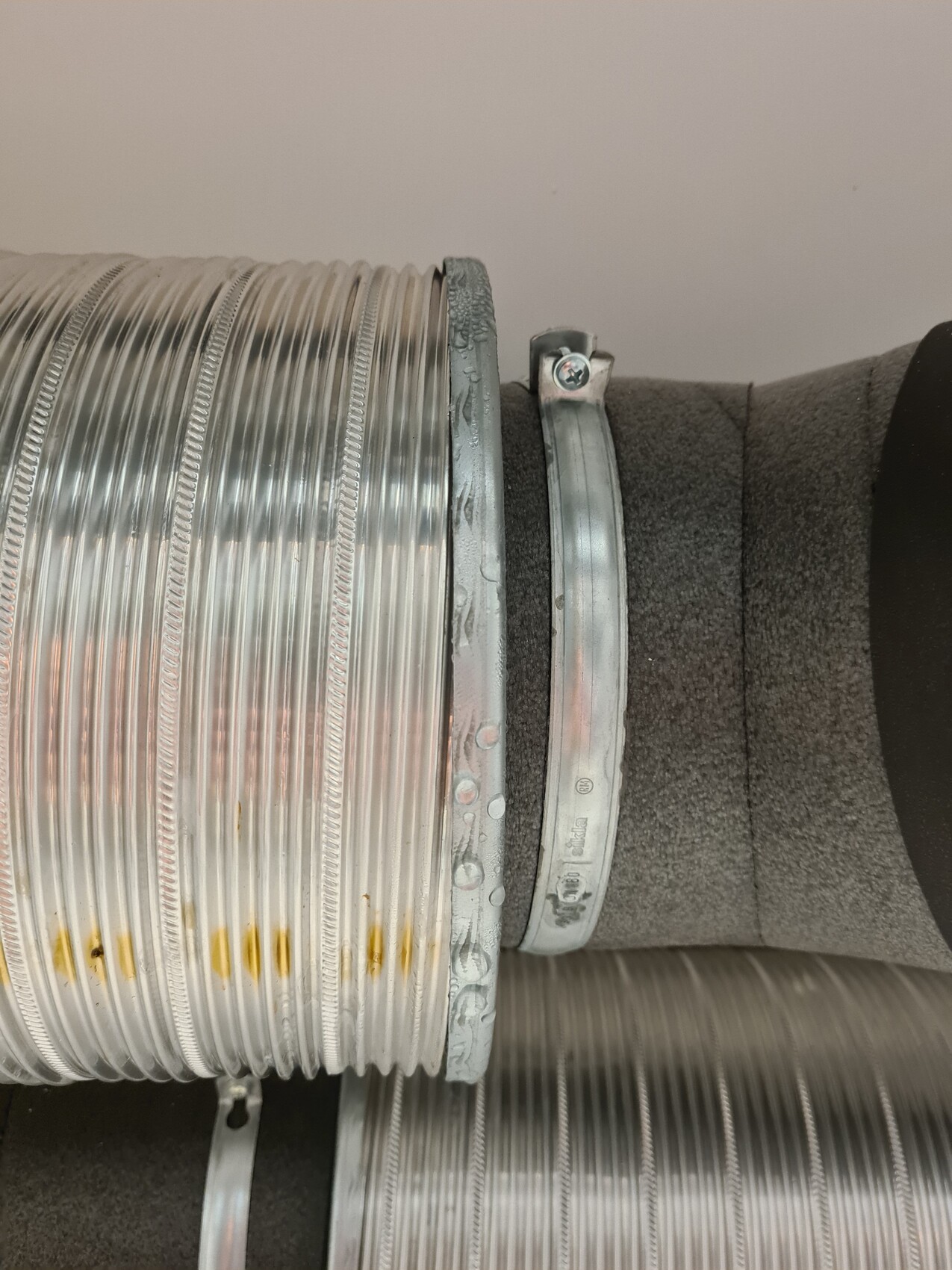 Spiral metal ventilation hose with clamp and insulation, mounted sideways.