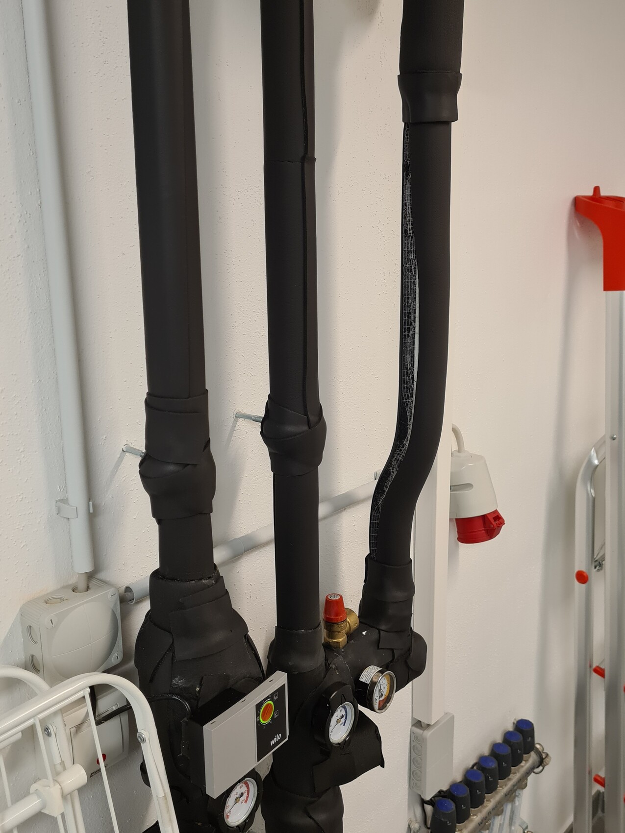 Several black insulated pipes with pressure gauges and valve knob in the heating room.