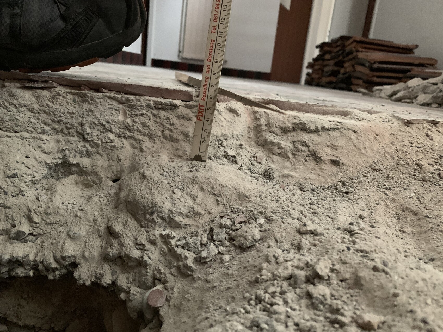 Close-up of a work boot on crumbly concrete; tape measure standing vertical.