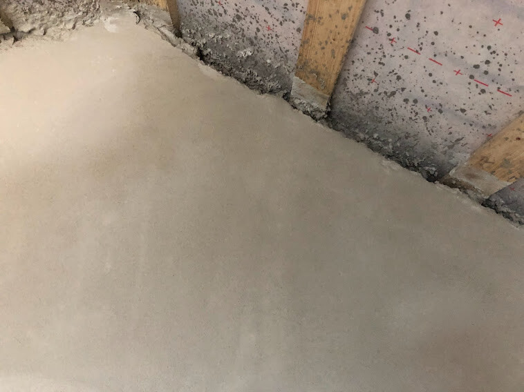 Smooth concrete floor in a shell construction; concrete wall with wooden supports.