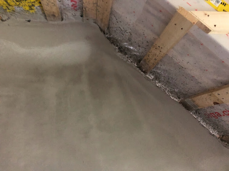Freshly poured concrete floor in a shell structure, wooden formwork at the wall.