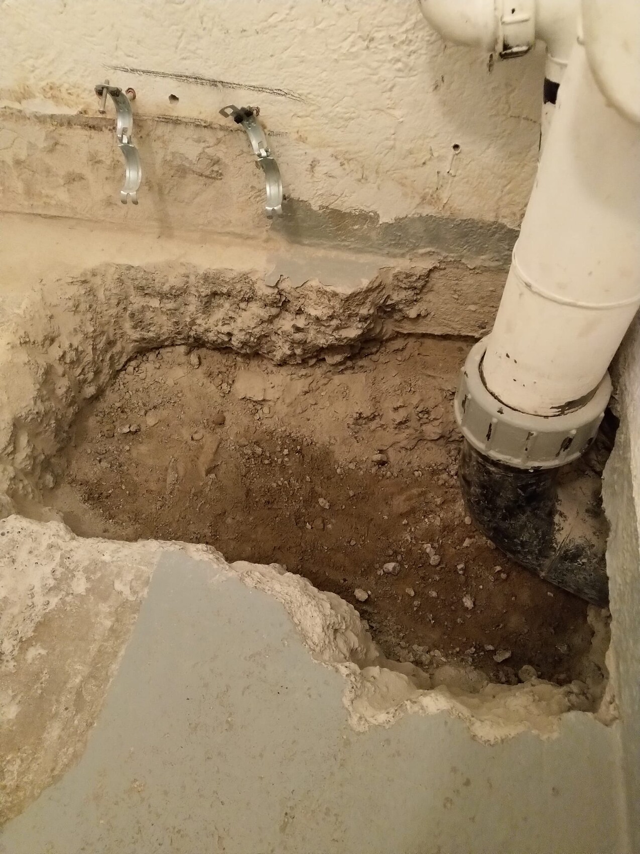 Open pit in the basement floor with exposed drain pipe and wall brackets.