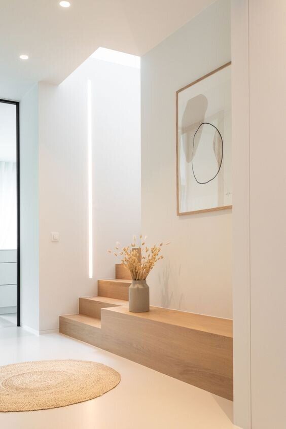 Modern entrance area with wooden steps, vase with dried flowers, LED light strips and wall art.