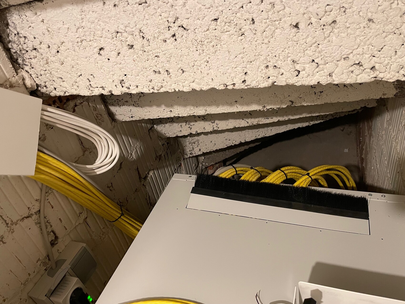 Bundles of yellow cables and white cables next to a white technical panel in a basement-like room.