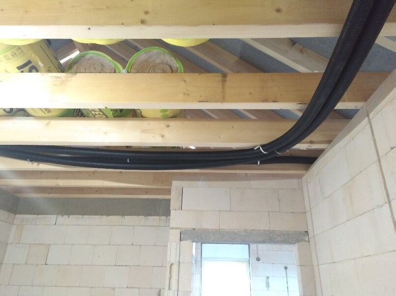 Construction site with timber beam ceiling, rolls of insulation material and black cable conduits along the ceiling.