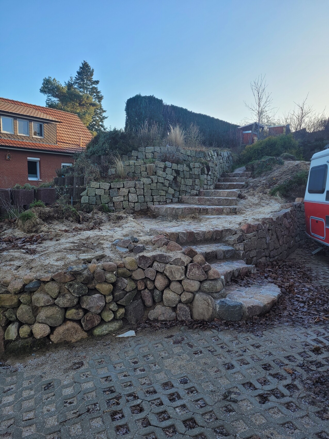 Natural stone stairs and dry stone wall in front of a house with a red tiled roof; caravan on the right.