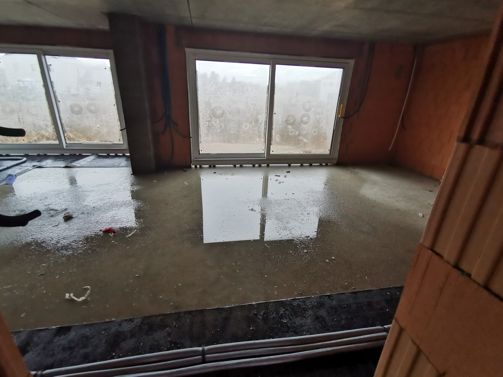 Unplastered interior space at construction site with standing water puddle, large glass doors to the exterior